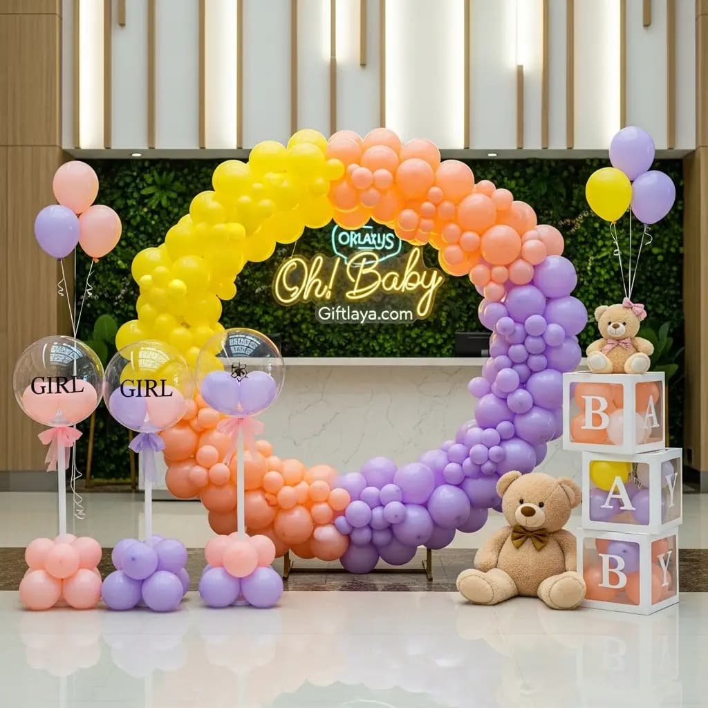 Baby shower setup with vibrant balloon arch in orange, yellow, and purple, “Oh! Baby” neon sign, transparent balloons labeled “GIRL,” and teddy bear on “BABY” blocks.